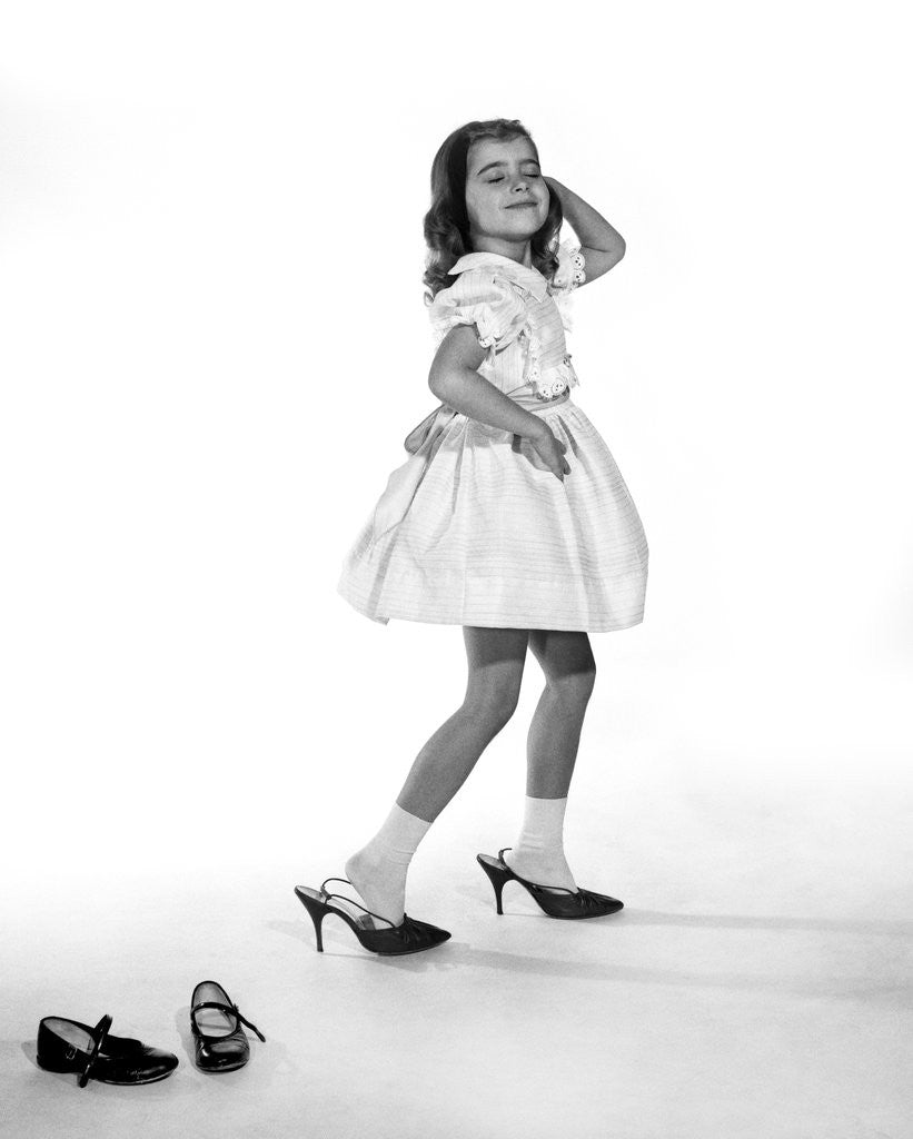 Detail of 1960s girl making glamour pose having stepped out of her shoes into her mothers adult high heels by Corbis