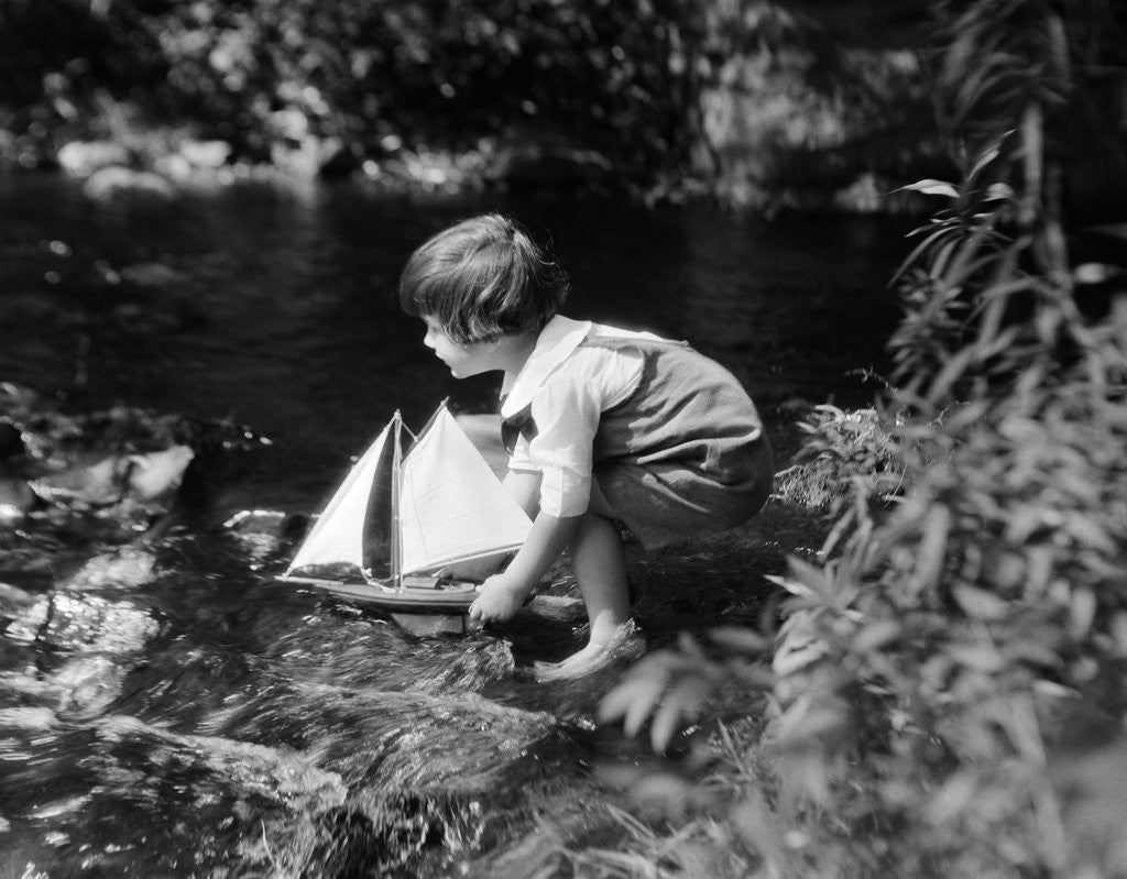 Detail of 1920s boy putting toy sailboat into stream by Corbis