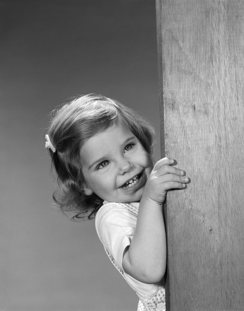 Detail of 1960s child little girl smiling peeking around corner by Corbis