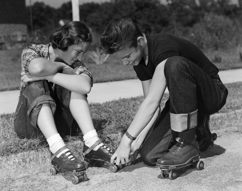 Detail of 1950s teen boy helping girl put on metal roller skates sitting on sidewalk by Anonymous