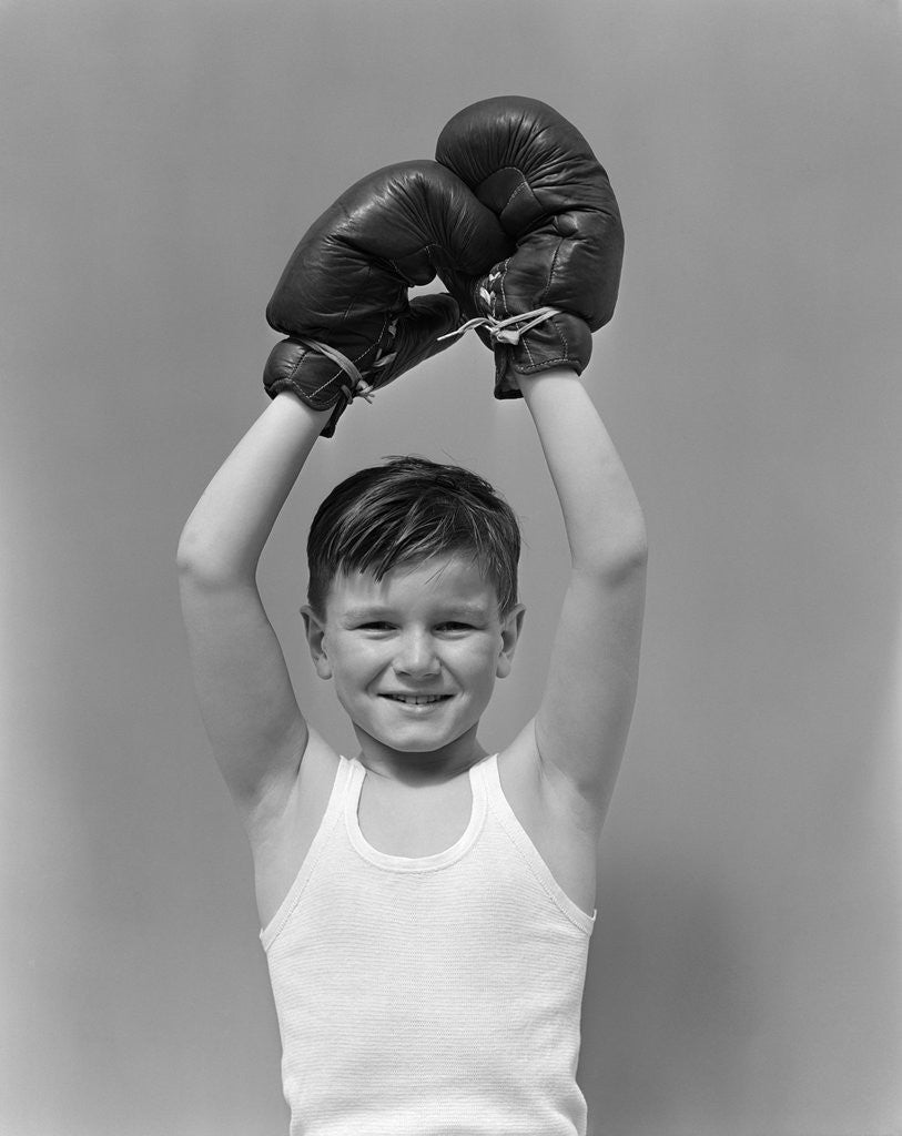 Detail of 1940s boy child winner wearing boxing gloves holding hands above head looking at camera by Corbis