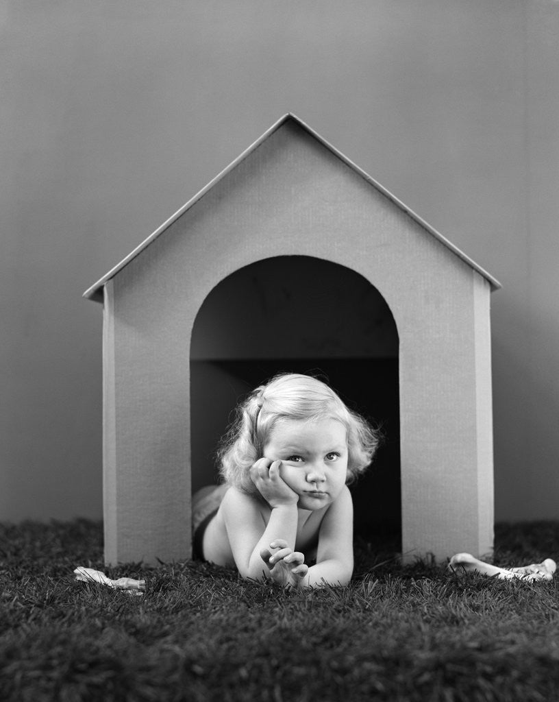 1940s girl in dog house lying on grass looking at camera by Corbis