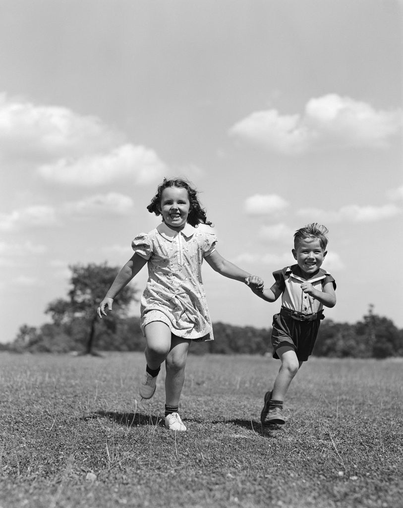 Detail of 1940s two smiling children running holding hands in grassy field by Anonymous