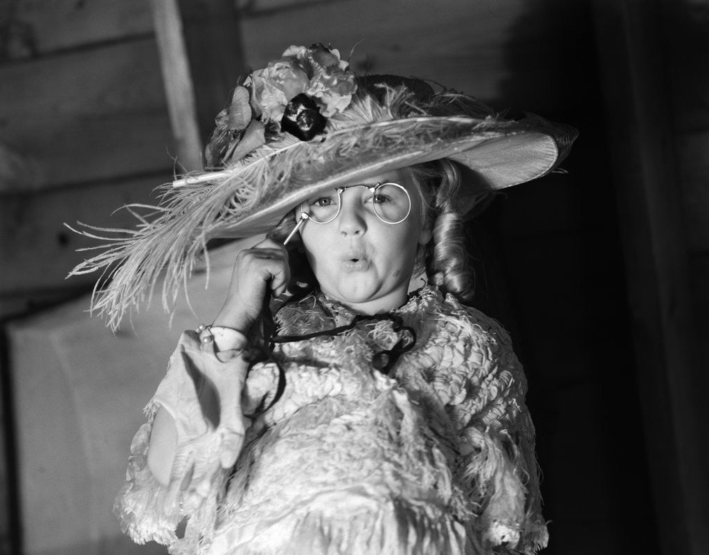 Detail of 1950s girl play dress up in her mothers clothes hat glasses spectacles facial expression role playing age aging by Anonymous