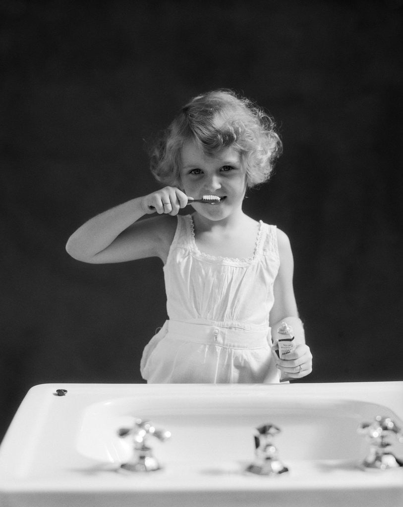Detail of 1930s child curly hair blond girl brushing teeth toothbrush looking at camera by Anonymous