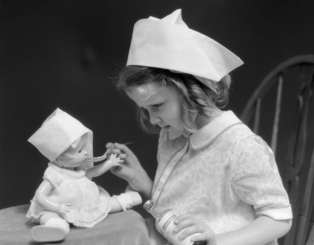 Detail of 1930s little girl playing nurse with doll spoonful of medicine by Anonymous