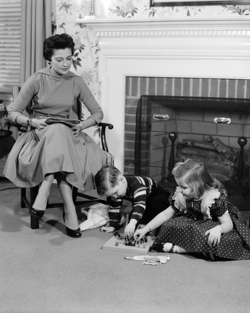 Detail of 1950s mother watching son daughter playing game in front of fireplace by Anonymous