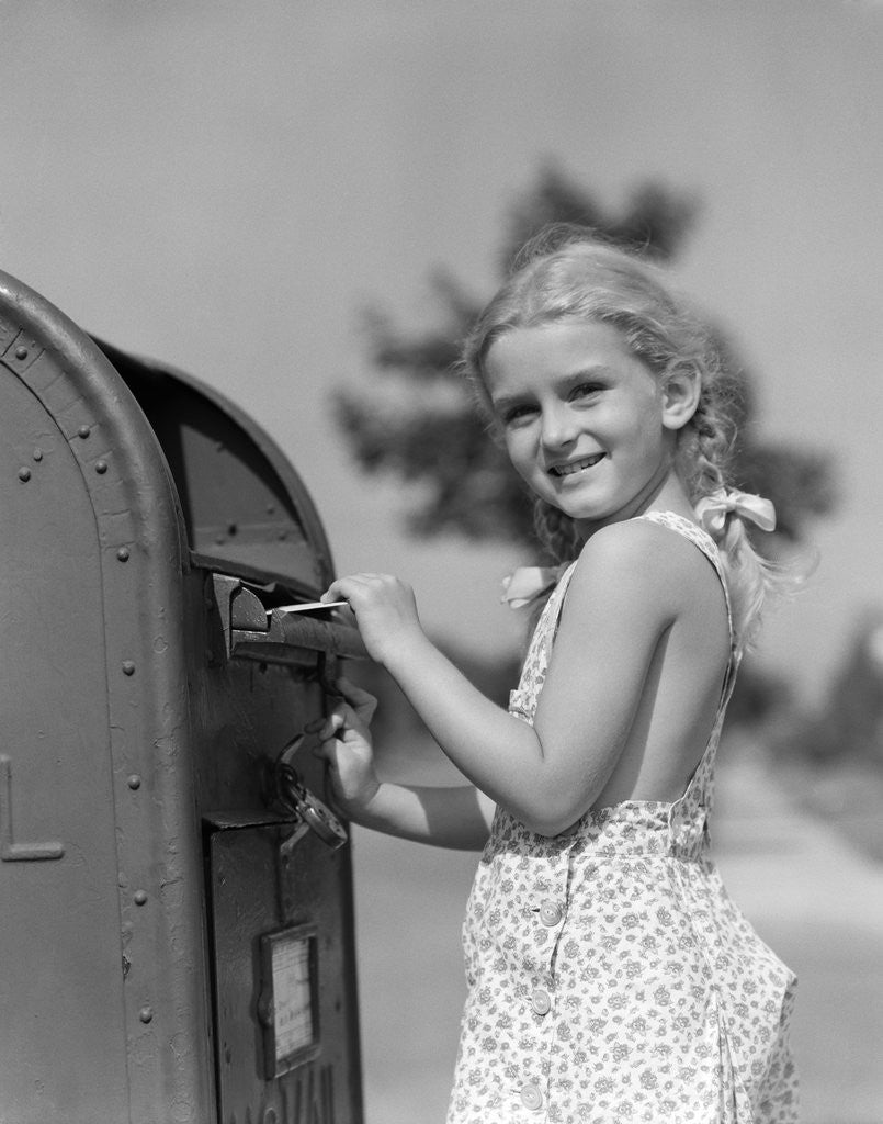 Detail of 1930s 1940s child blond little girl with pigtails putting letter into mail box, looking at camera by Anonymous