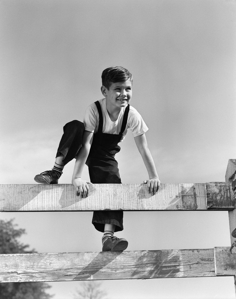 Detail of 1940s brunette boy wearing overalls climbing over fence by Anonymous