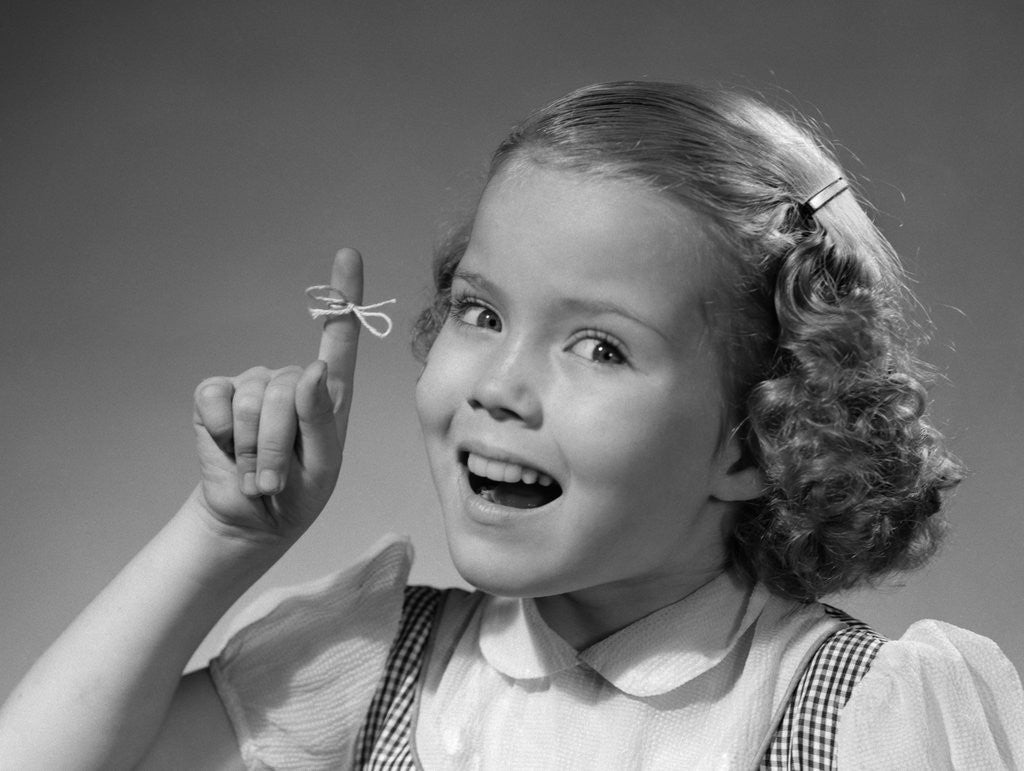 Detail of 1950s little girl string tied on finger as reminder not to forget smiling looking at camera by Anonymous