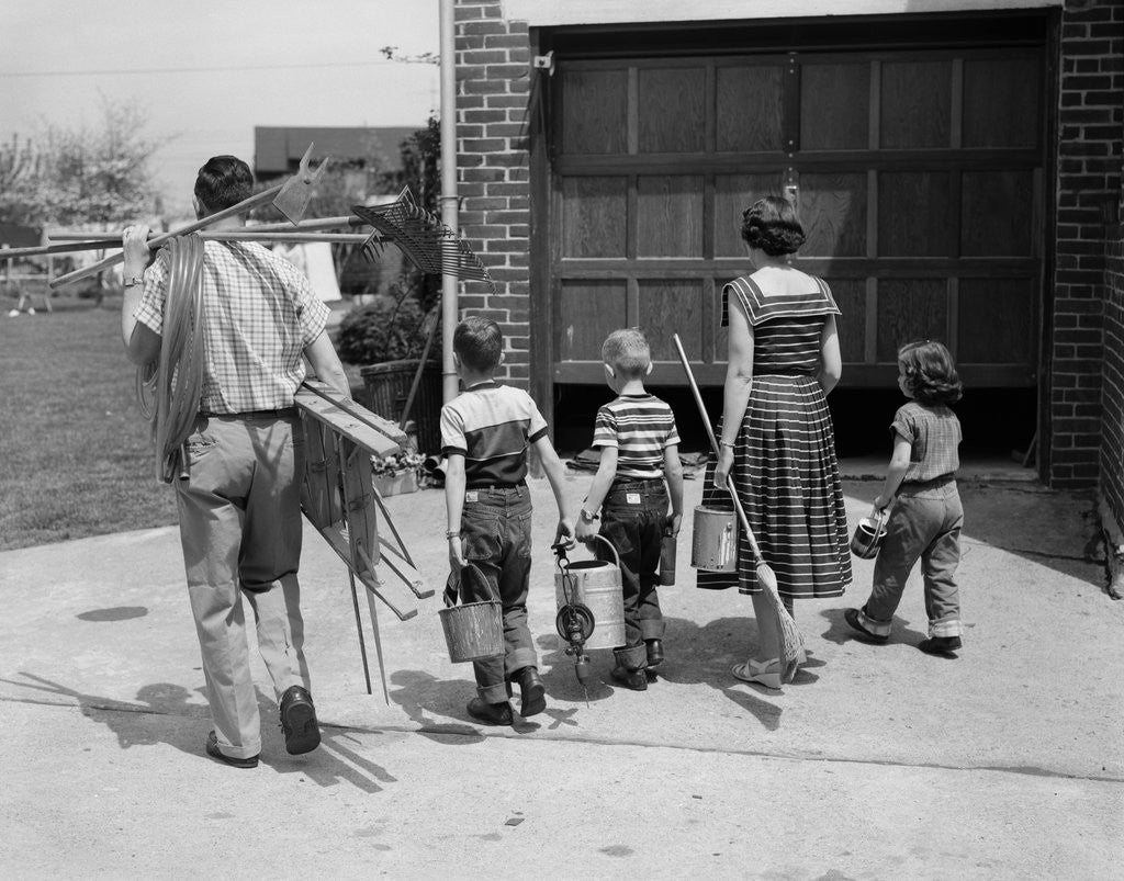 Detail of 1950s family mother father 3 children from behind carrying gardening home improvement tools equipment by Anonymous
