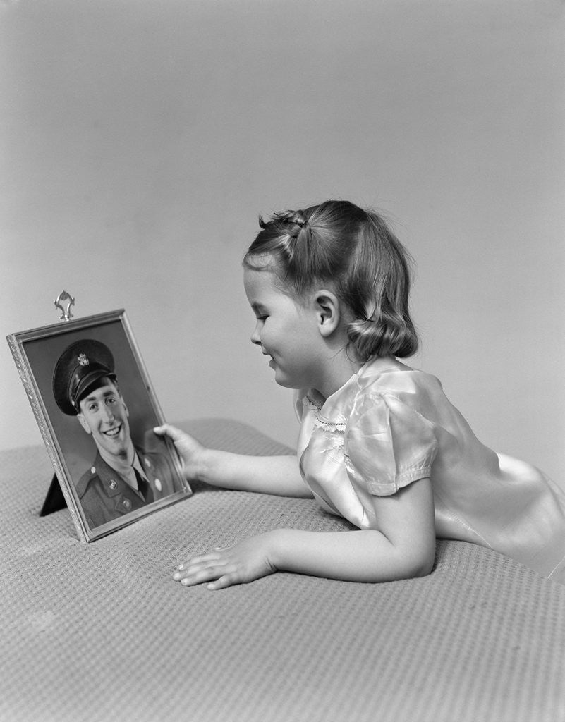 Detail of 1940s child little girl looking at framed picture of her father a soldier in uniform by Anonymous