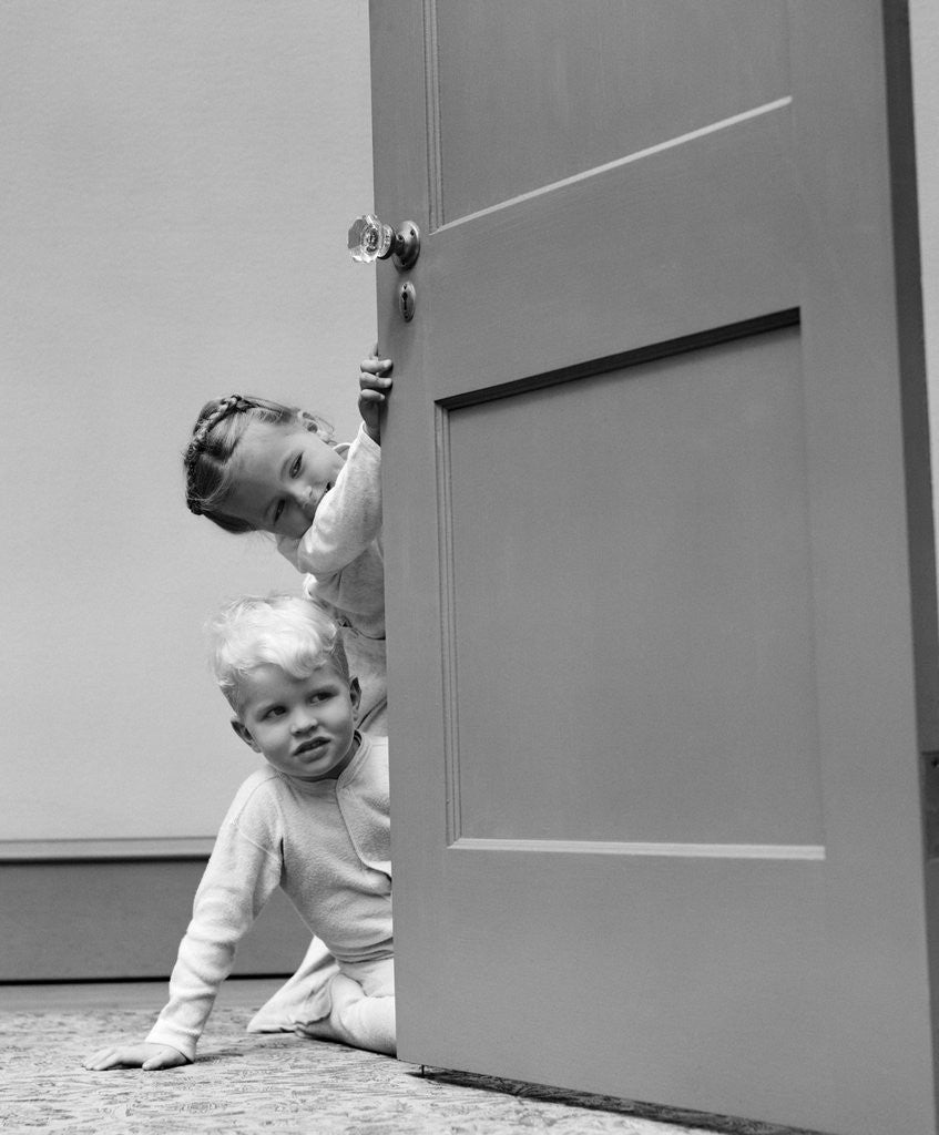 Detail of 1940s children boy and girl in pajamas peeking around door by Corbis