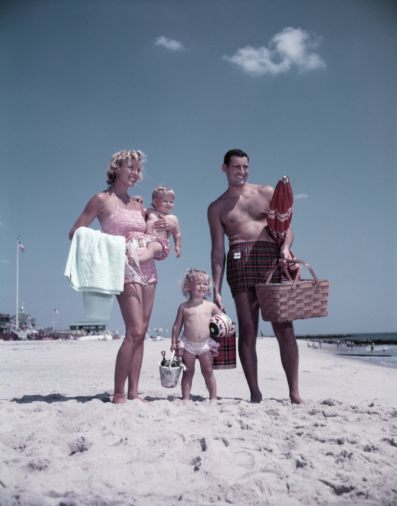 Detail of 1950s family man woman mother father children boy girl son daughter standing sandy beach with toys and picnic basket by Anonymous