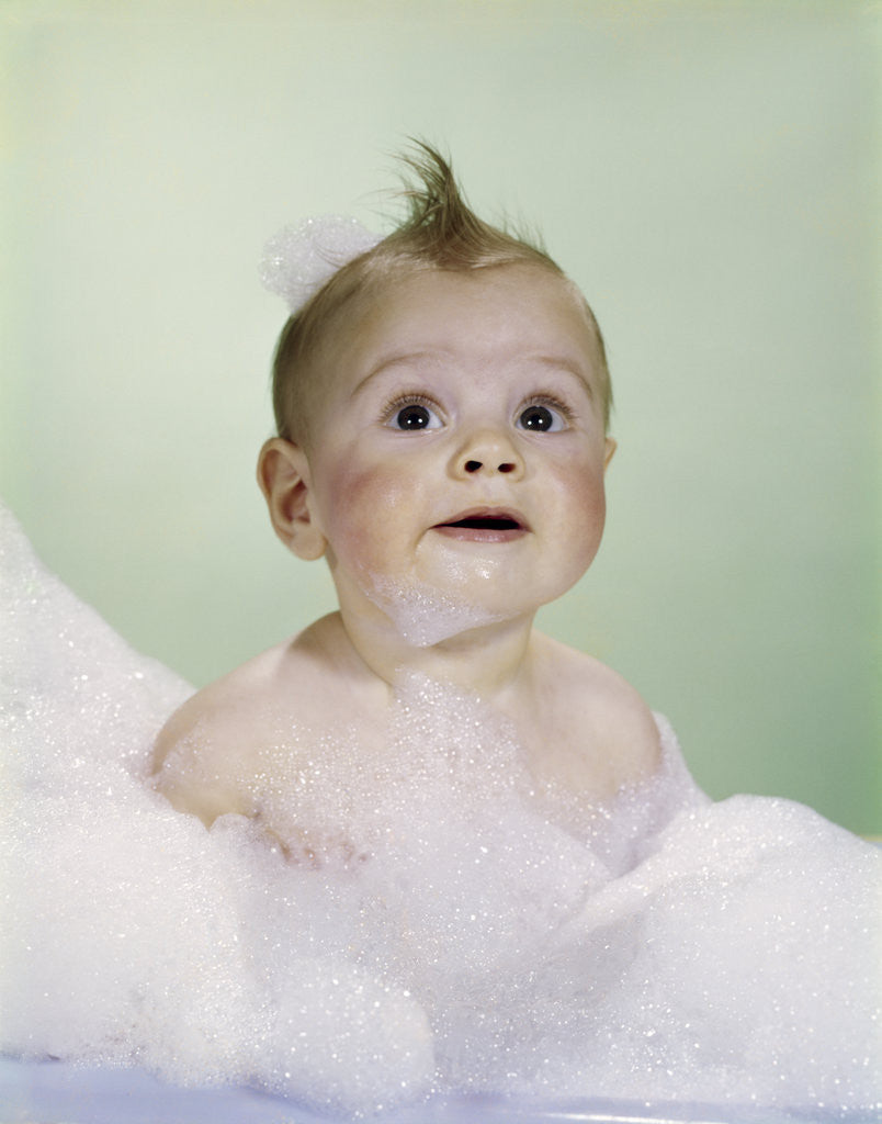 Detail of 1960s baby sitting in bath surrounded by suds by Anonymous