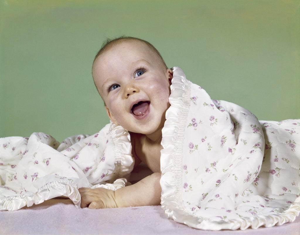 Detail of 1960s smiling happy baby peeking out from under a blanket by Anonymous