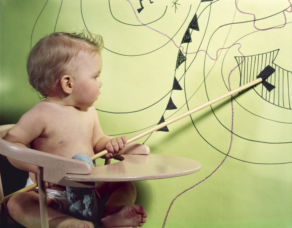 Detail of 1960s baby in high chair using wooden pointer to indicate low pressure area on weather map by Corbis