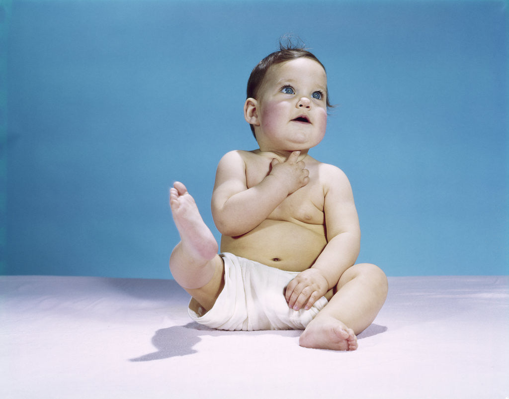 Detail of 1960s baby wearing diaper sitting looking up and kicking one leg up by Anonymous
