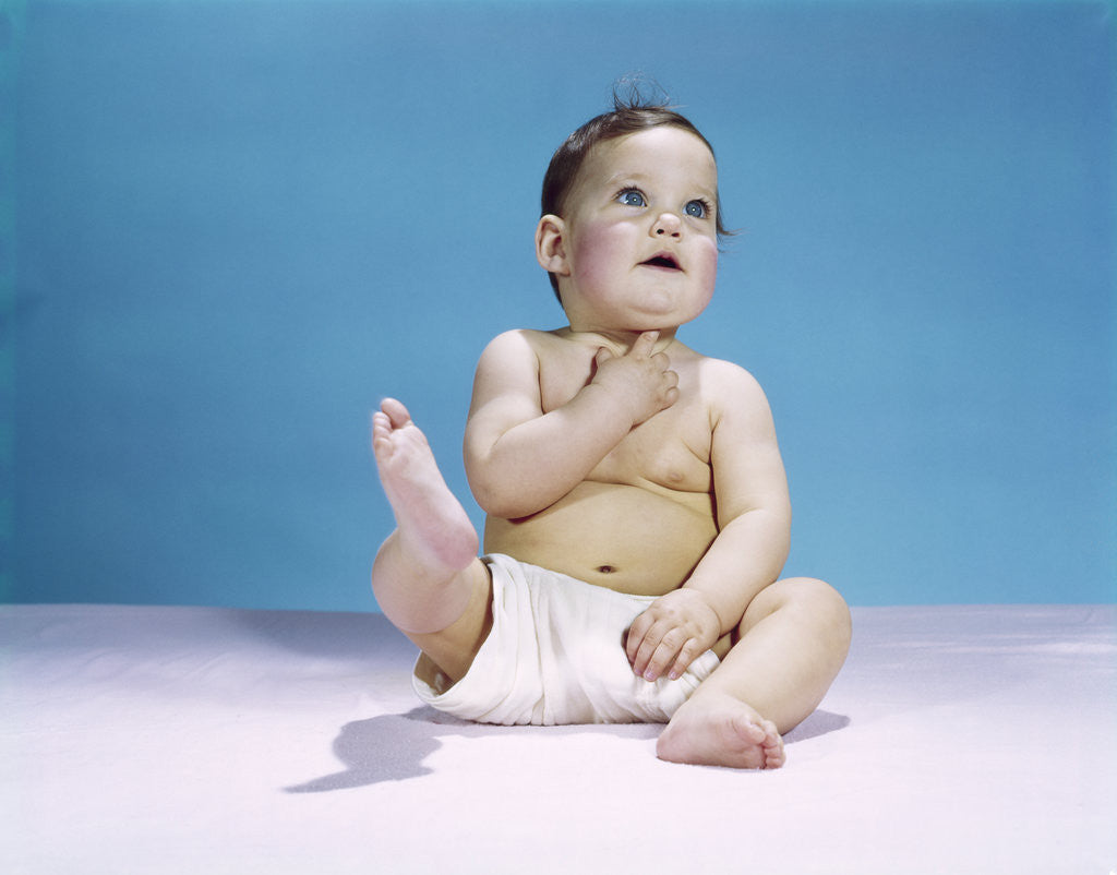 Detail of 1960s baby wearing diaper sitting looking up and kicking one leg up by Corbis