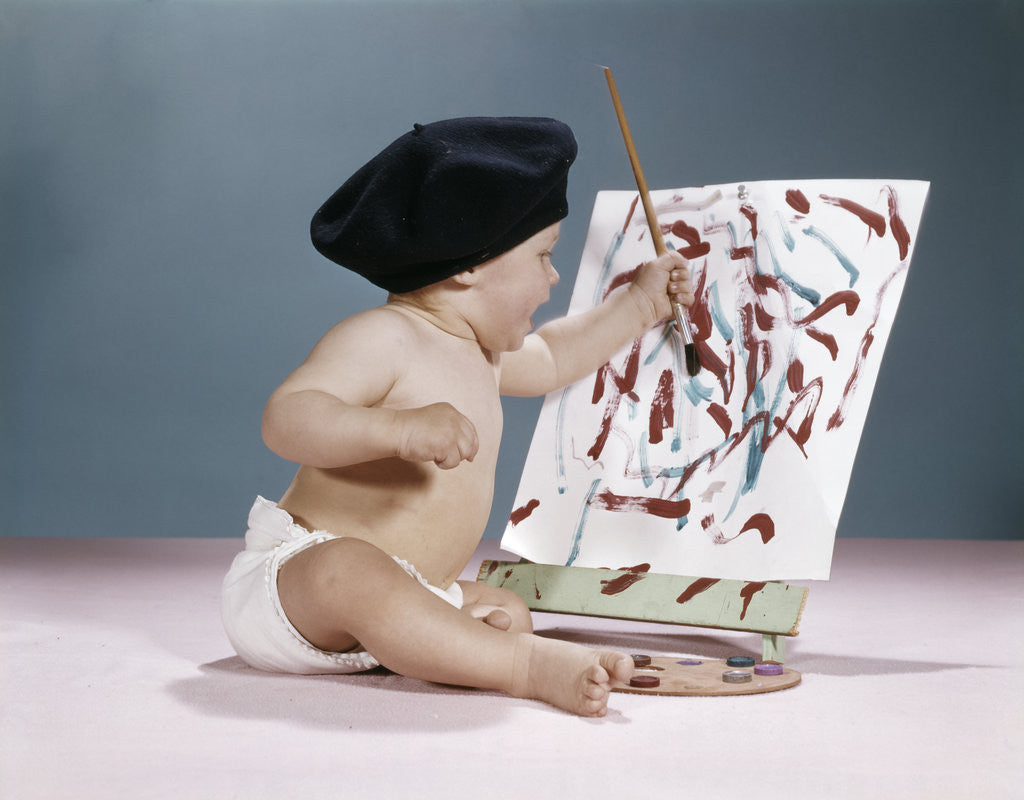 Detail of 1960s baby artist wearing black beret sitting in front of easel painting by Corbis