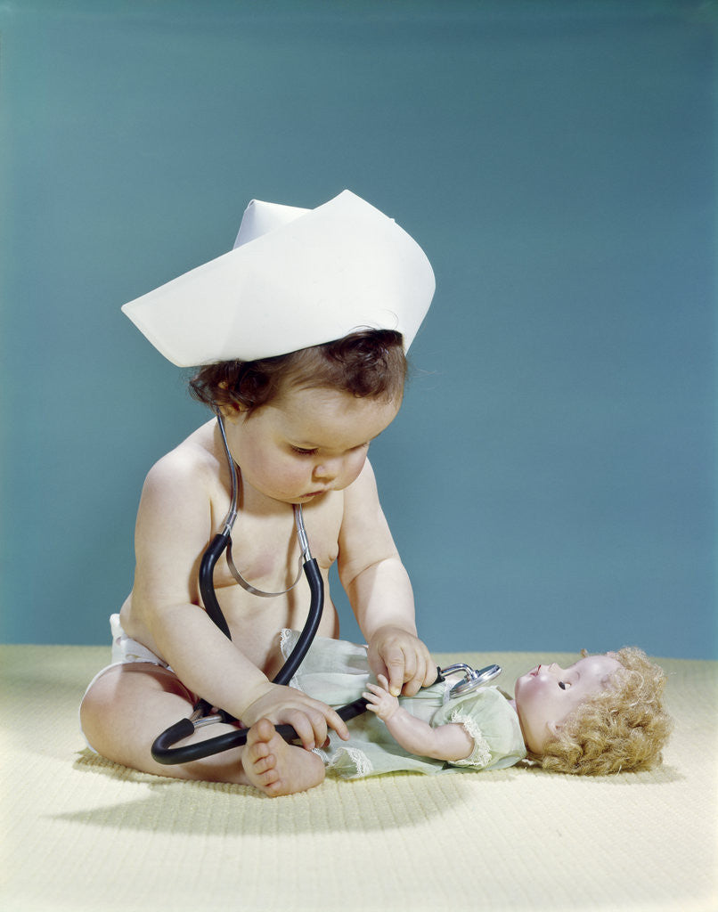 Detail of 1960s baby wearing nurse nurse's cap stethoscope listening to doll heartbeat chest by Anonymous