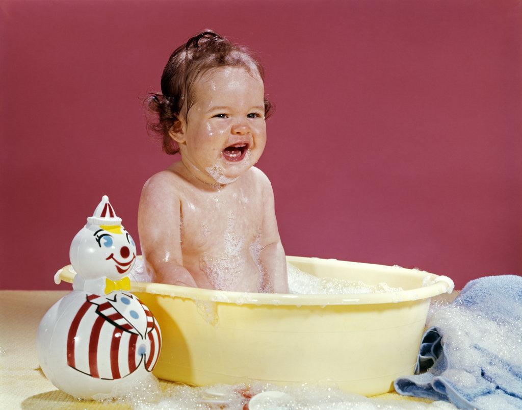 Detail of 1960s crying brunette baby sitting in yellow plastic bath tub with toy clown by Anonymous