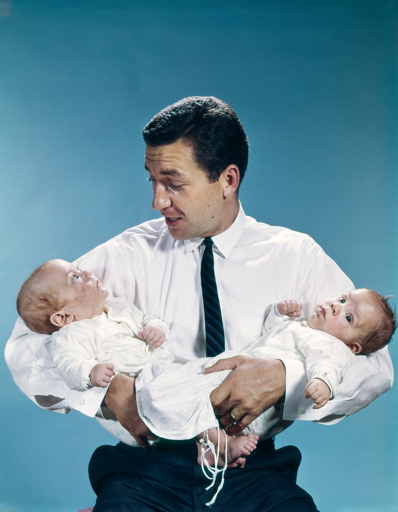Detail of 1960s father holding twin babies infants looking down at one of them by Corbis