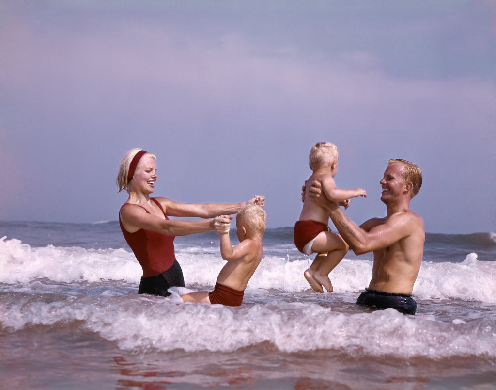 Detail of 1970s family father mother two sons laughing hand holding jumping in ocean surf at beach having fun together by Corbis