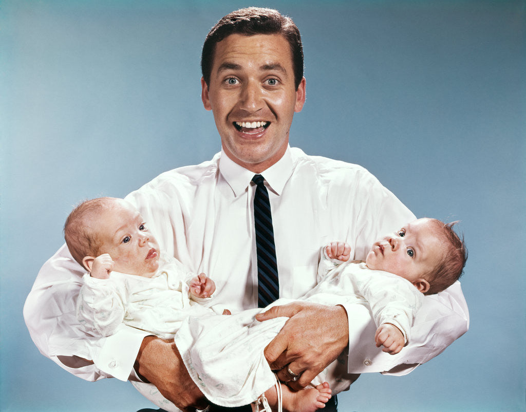 Detail of 1960s smiling man father looking at camera holding twin babies infants by Anonymous