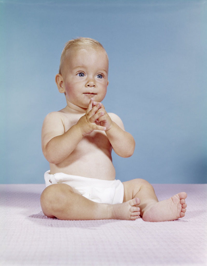 Detail of 1960s baby wearing cloth diaper sitting with hands together thoughtful pose expression by Anonymous