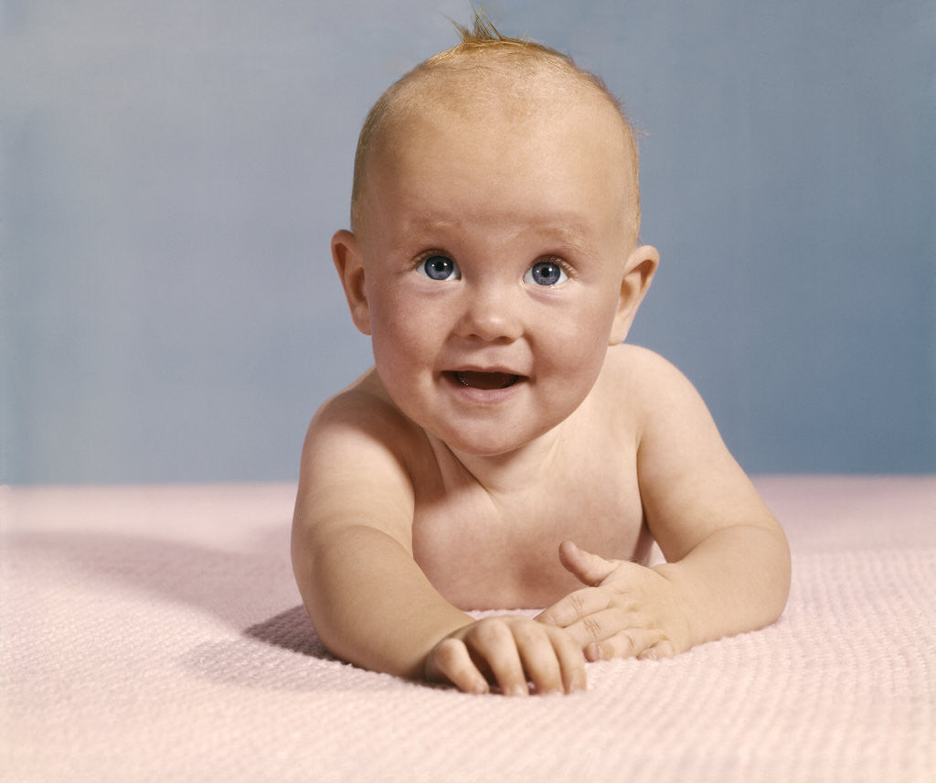 Detail of 1970s smiling happy baby crawling straight ahead on pink blanket looking at camera by Anonymous