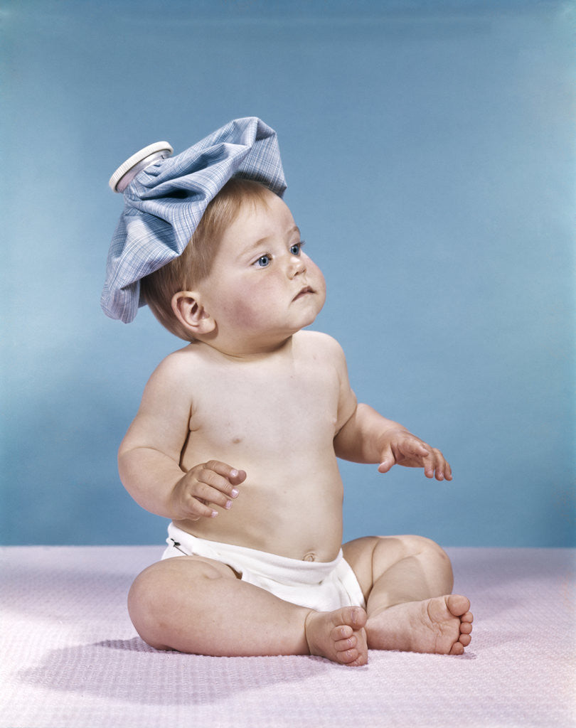 Detail of 1960s baby sitting with ice pack on top of head by Anonymous