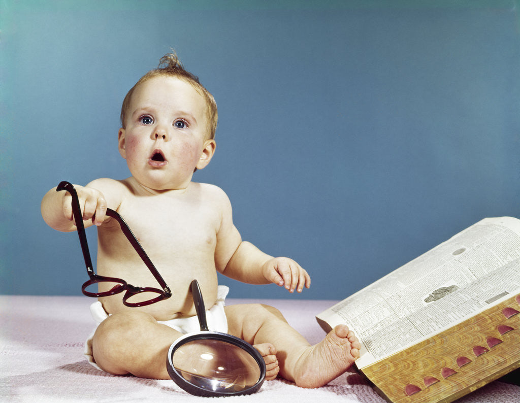 Detail of 1960s baby holding eyeglasses with open dictionary and magnifying glass research by Anonymous