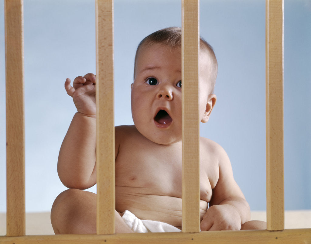 Detail of 1960s baby in crib or playpen looking through bars alarmed expression by Anonymous