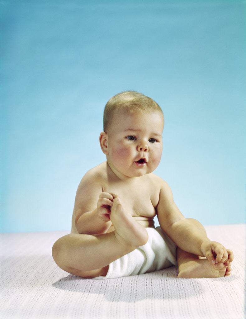 Detail of 1960s baby sitting holding on to his feet by Anonymous