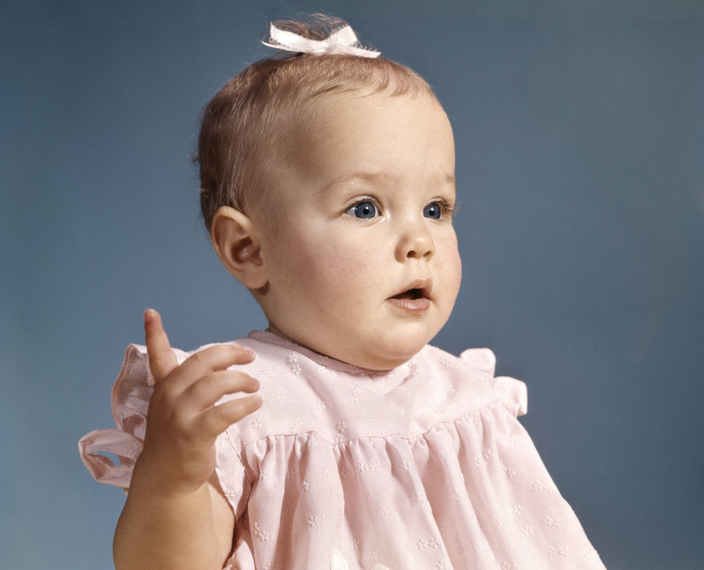 Detail of 1960s baby girl wearing pink dress with a bow in her hair pointing a finger by Anonymous
