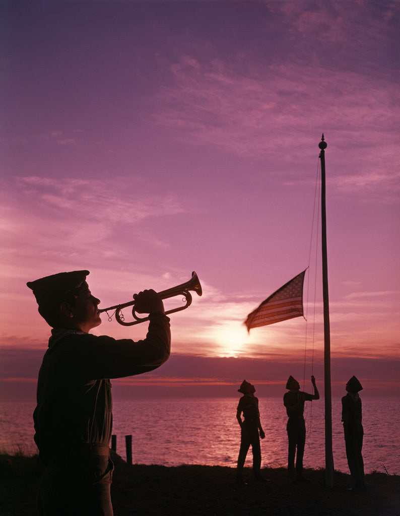 Detail of 1960s boy scout blowing bugle as others raise american flag at camp sunset ceremony by Anonymous
