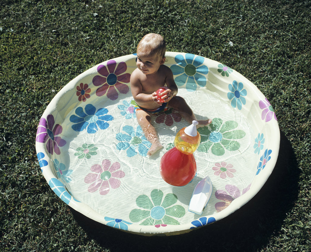 Detail of 1970s baby sitting in plastic backyard kiddy pool viewed from above by Anonymous
