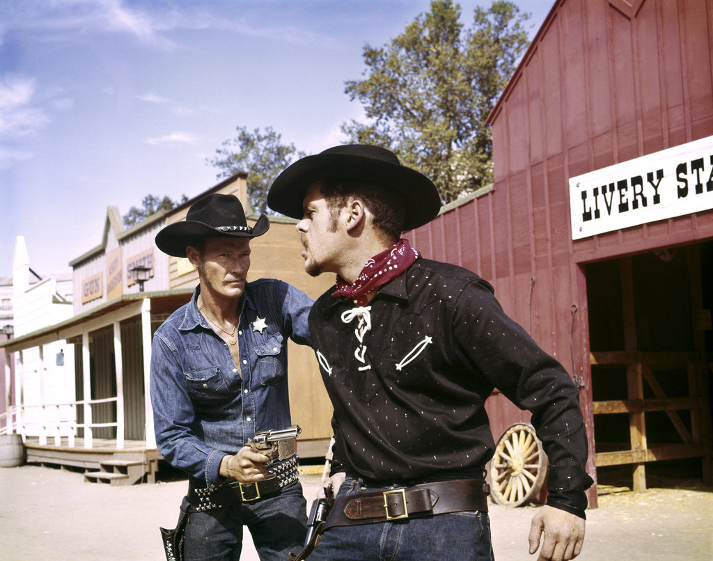 Detail of 1960s cowboy sheriff with badge draws gun arrests gunfighter in front of livery stable by Anonymous