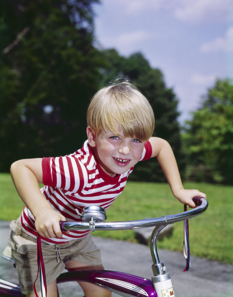 Detail of 1970s 1960s smiling blond boy leaning over handlebars of bicycle looking at camera by Anonymous