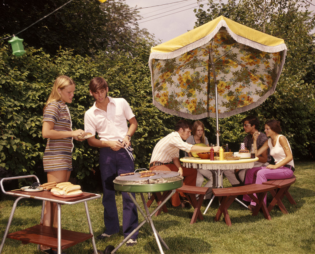 Detail of 1970s group teenagers boys girls backyard grilling table umbrella by Corbis