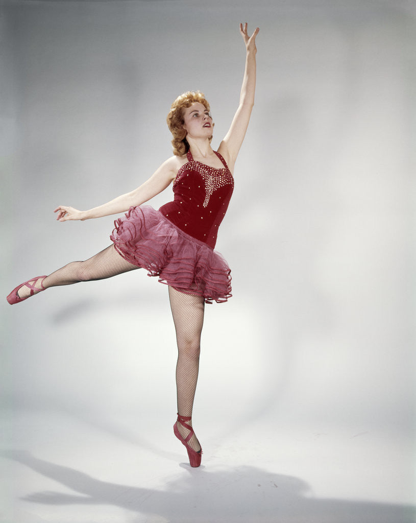 Detail of 1960s awkward teen girl red velvet costume pink net tutu attempting arabesque en pointe by Corbis