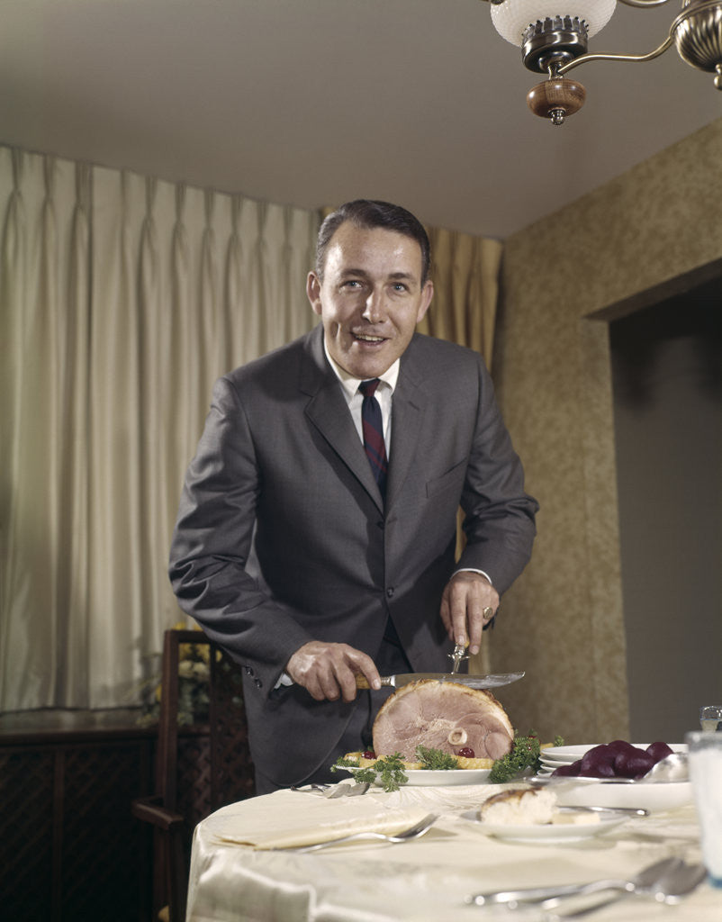 Detail of 1960s man carving ham dinner looking at camera by Anonymous