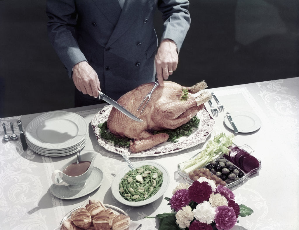 1950s male hands about to carve thanksgiving turkey table setting plates gravy rolls olives crudities by Corbis