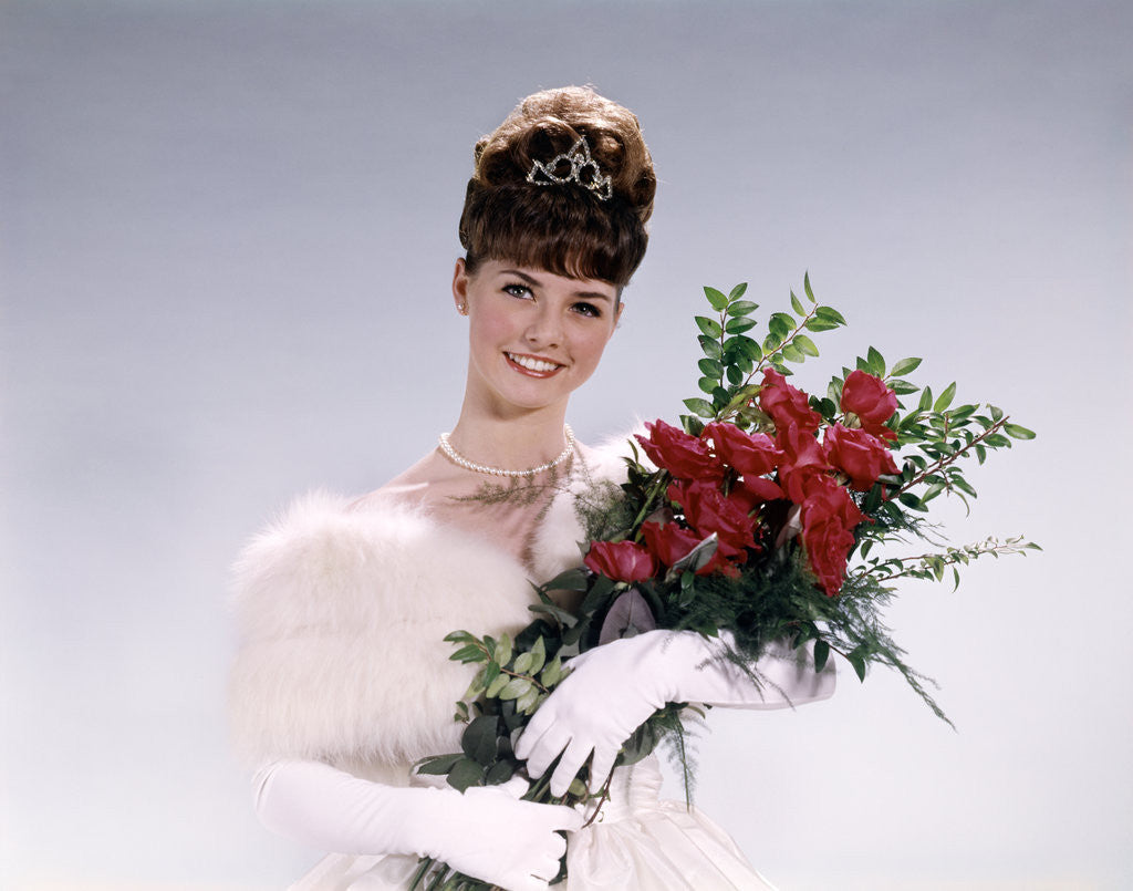 Detail of 1960s woman prom queen wearing white evening dress holding bouquet of flowers red roses looking at camera by Anonymous