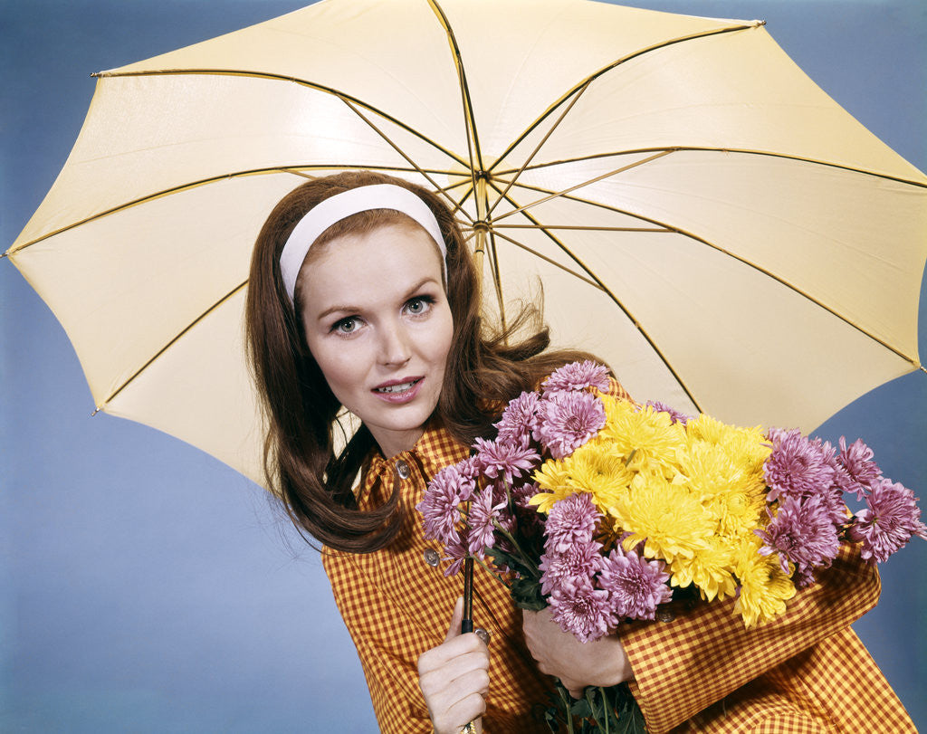 Detail of 1960s smiling brunette woman holding bouquet autumn flowers chrysanthemums under umbrella red yellow rain coat by Corbis