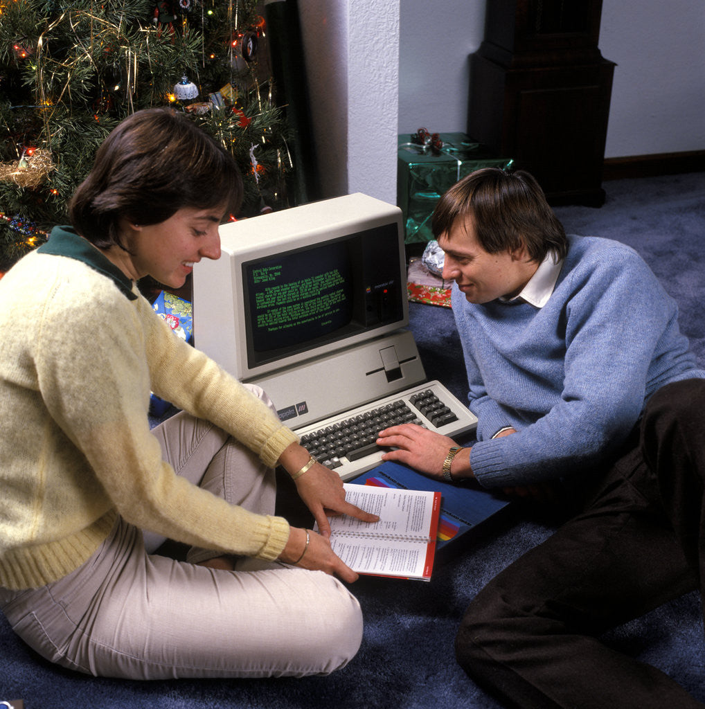 Detail of 1980s couple by christmas tree reading instructions for an apple iii computer by Corbis