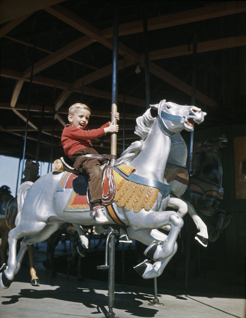 Detail of 1950s excited boy riding carved wooden carousel merry-go-round horse by Anonymous