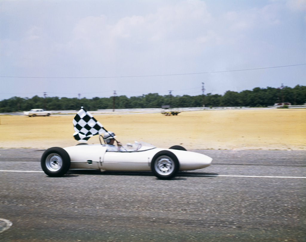 Detail of 1960s race car driver in lotus ford car taking victory lap holding checkered flag by Corbis