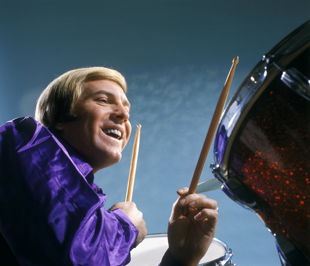 Detail of 1970s laughing blond man musician playing drums wearing purple shirt by Anonymous